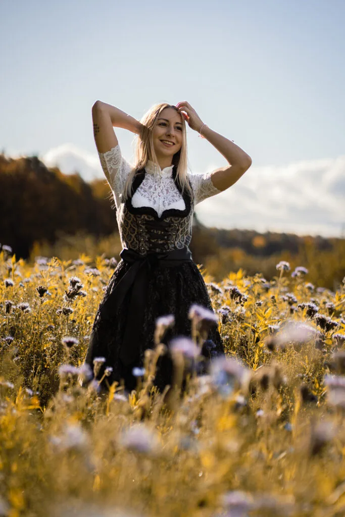Frau in einem eleganten schwarzen Dirndl mit weißer Spitzenbluse auf einer Blumenwiese