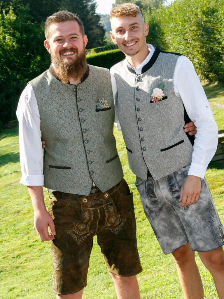 Zwei Männer in festlichen grauen Trachtenwesten und Lederhosen bei einer Feier im Garten